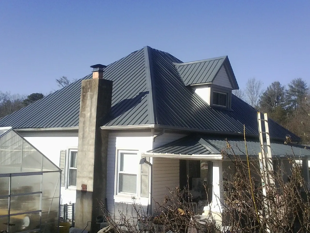 Dark blue standing seam metal roof on a white farmhouse with dormer — Slate & Tile Roof Repair by Roofing Brothers in Jeremiah
