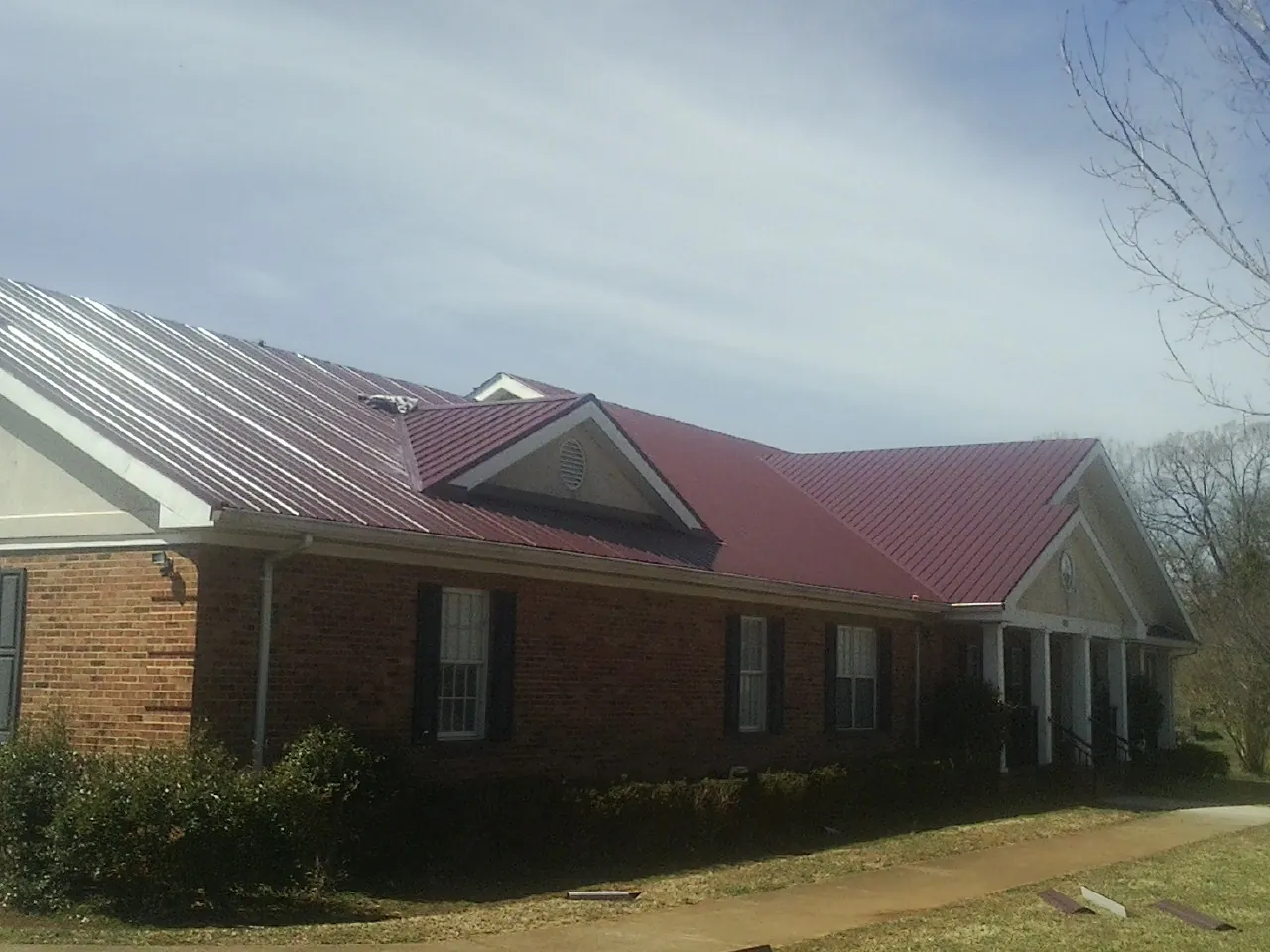 Red metal roof with gabled entries on a long brick building, from a Hail Damage Roof Repair job in Jeremiah