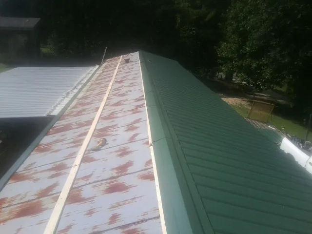 Old rusted panels beside newly installed green metal roofing — Wind Damage Roof Repair by Roofing Brothers in Jeremiah