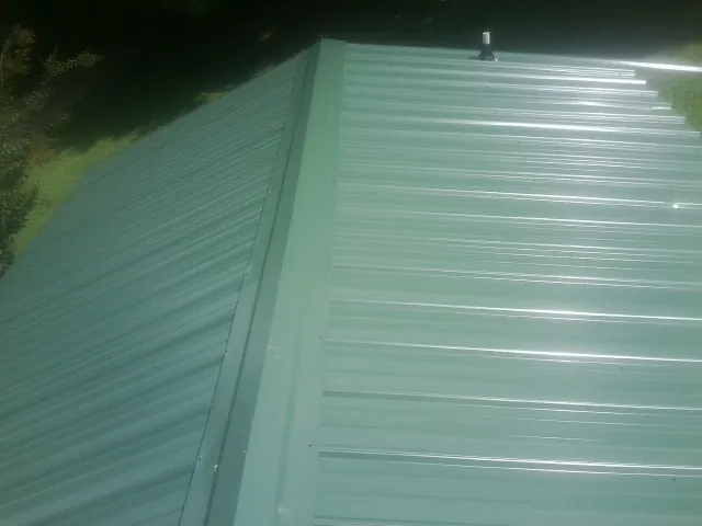New green metal panels meeting at the ridge of a roof — Flat Roof Repair work by our crew in Jeremiah