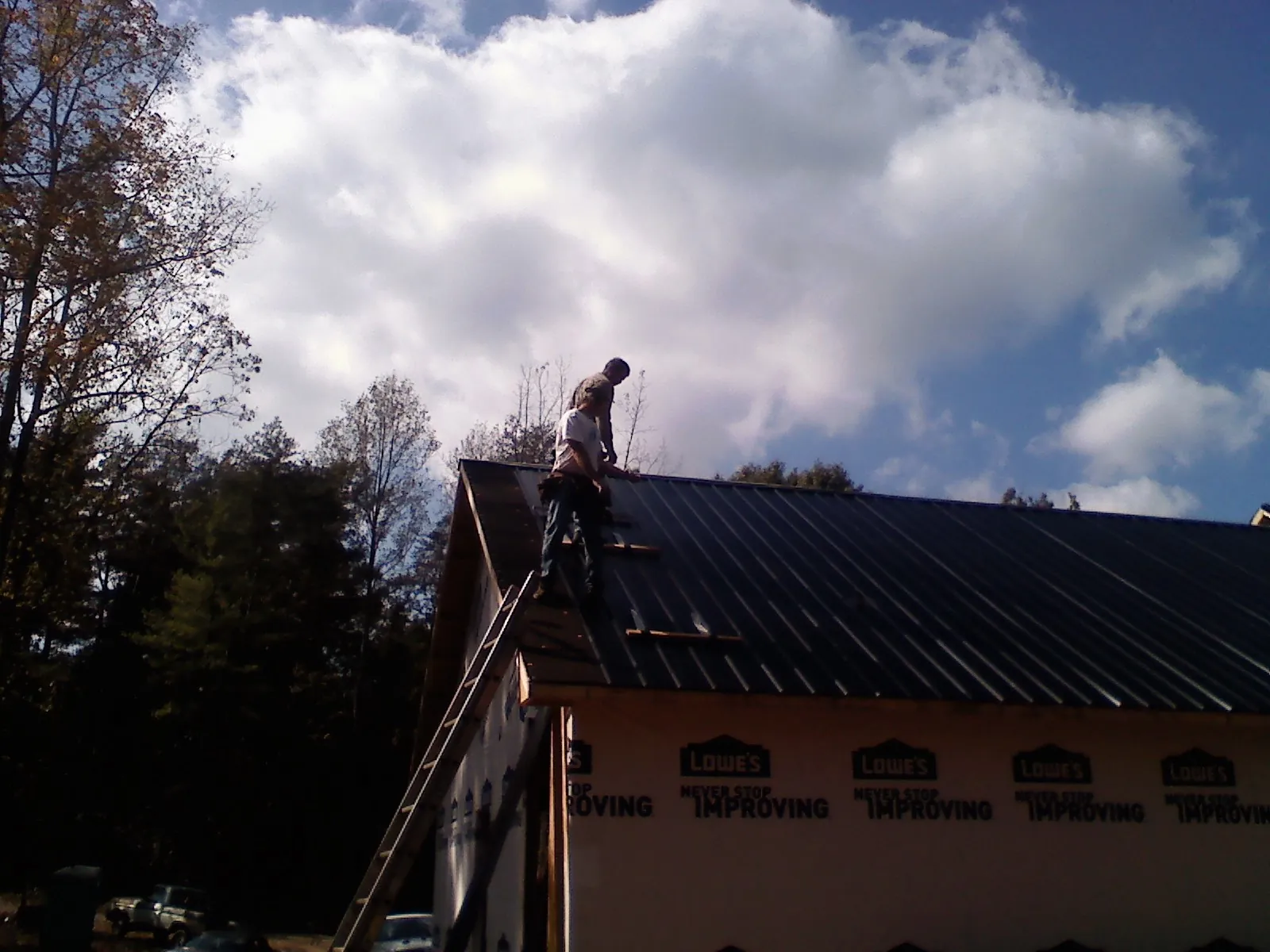 Roofer fastening dark metal panels high against a cloudy sky, from a Roof Inspection job in Jeremiah