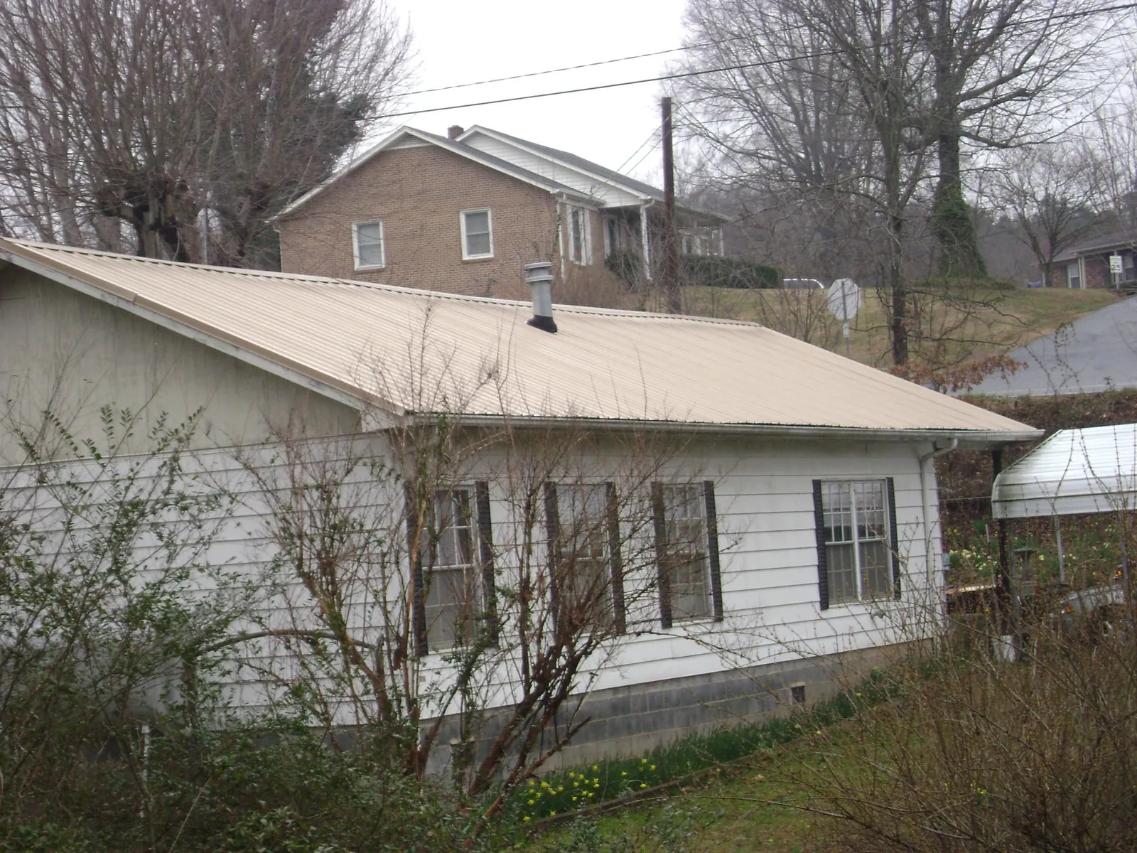 Tan metal roof on a white sided house set into a hillside — Commercial Roofing by Roofing Brothers in Jeremiah