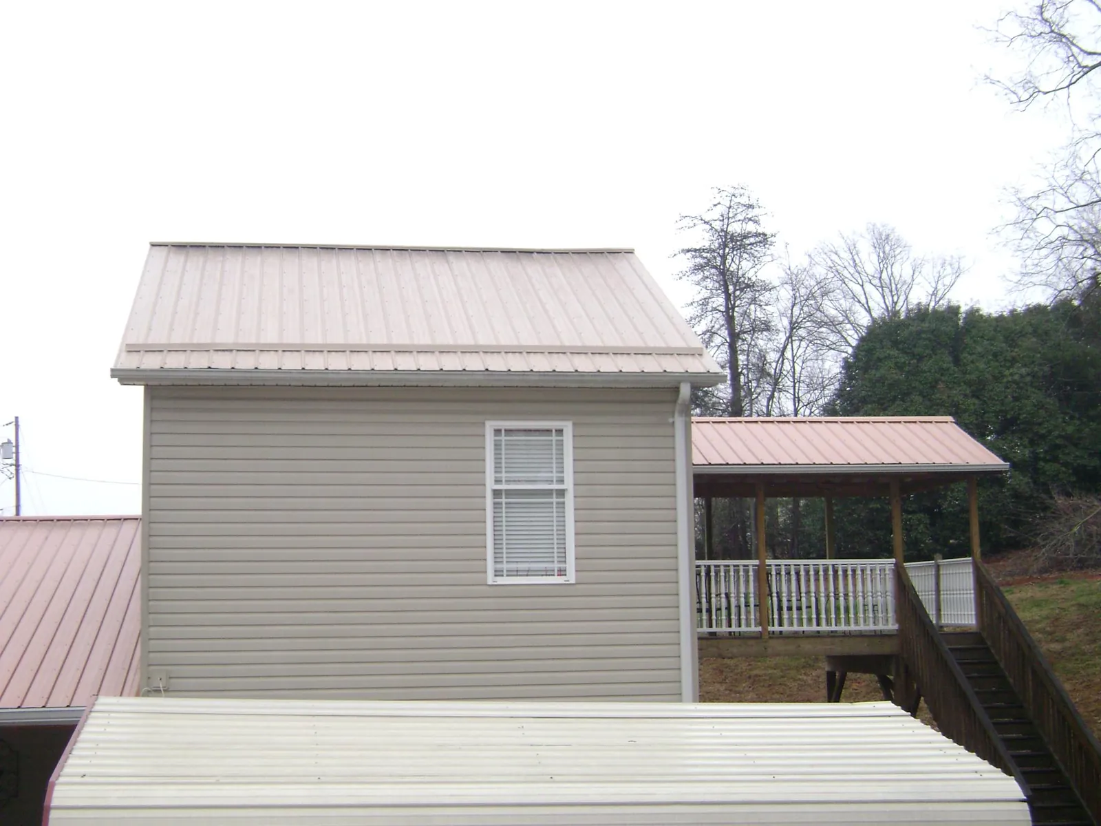 Tan metal roofs on a two story addition and attached porch, from a Roof Replacement job in Jeremiah